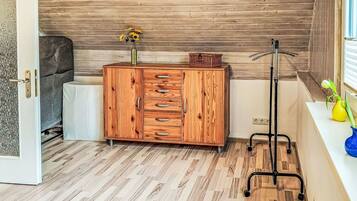 Un mueble de madera con cajones, un jarrón con flores y una lámpara de pie en una habitación con suelo de madera y una ventana.