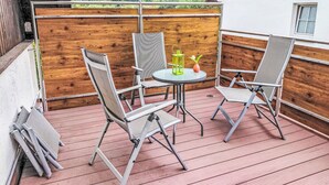 Un balcon avec deux chaises et une table, une clôture en bois et une vue sur une zone boisée.