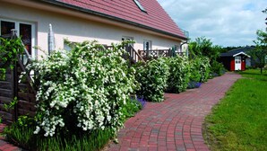 Une maison avec un toit rouge, un chemin en briques et des arbustes à fleurs blanches.