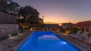 A rectangular swimming pool with a stone border, surrounded by lounge chairs and a stone patio.
