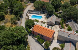 Vue aérienne d’une propriété dotée d’une piscine, de bâtiments en pierre et d’un environnement verdoyant.