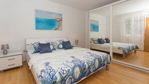 A bedroom with a bed, a nightstand, a mirror, and a painting of a coastal scene.