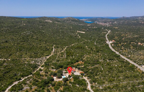 Vue aérienne d’une zone rurale, avec un marqueur rouge indiquant l’emplacement d’une propriété entourée de verdure et bordée d’une route sinueuse.