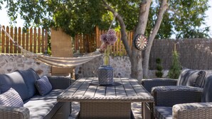 An outdoor seating area with wicker furniture, a central table, and a decorative vase with flowers.