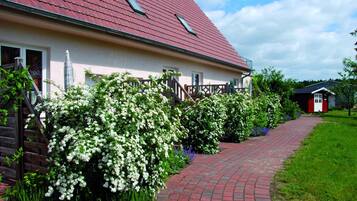 A house with a red roof, a brick pathway, and white flowering bushes.