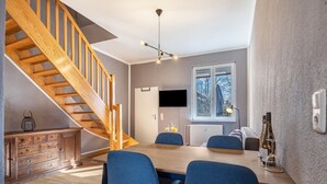 A modern kitchen with a wooden staircase, a dining table with blue chairs, and a TV mounted on the wall. - Komfortables Reihenhaus mit WLAN in Buchholz am Müritzsee (Buchholz am Müritzsee)