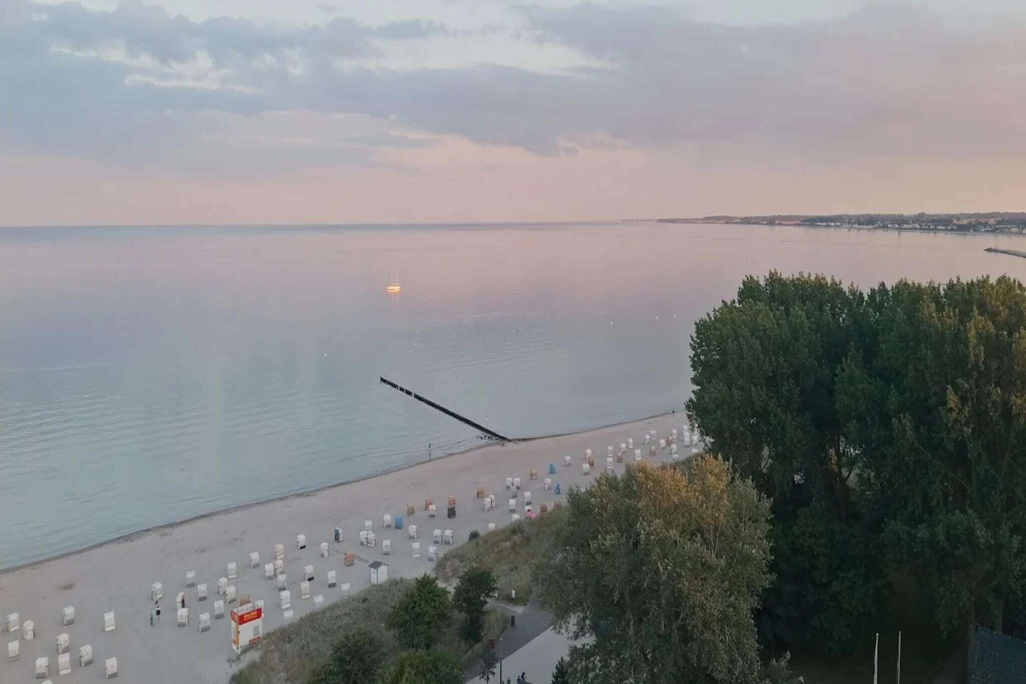 A beach with rows of white tents and a pier extending into calm waters.