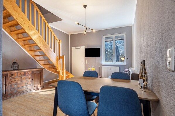 Une cuisine moderne avec un escalier en bois, une table à manger avec des chaises bleues et un téléviseur fixé au mur.