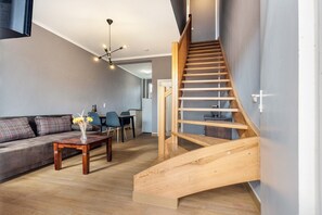 Un salon moderne avec un escalier en bois, un canapé, une table basse et, au fond, un coin repas.