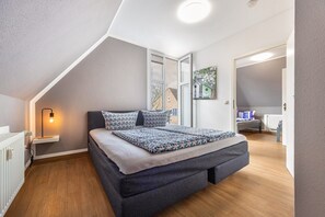 Une chambre de style loft moderne, avec un plafond en pente, un lit intégré, une table de chevet avec une lampe et une vue sur l’extérieur.