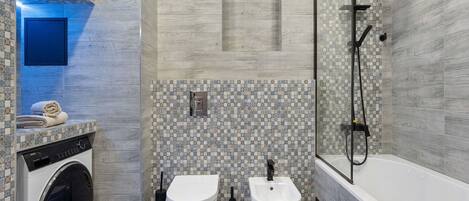 A modern bathroom with a washing machine, two toilets, a bidet, and a shower.
