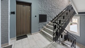 Interior moderno com porta de madeira marcada “425”, parede de pedra, escada com corrimão preto e uma pequena janela.