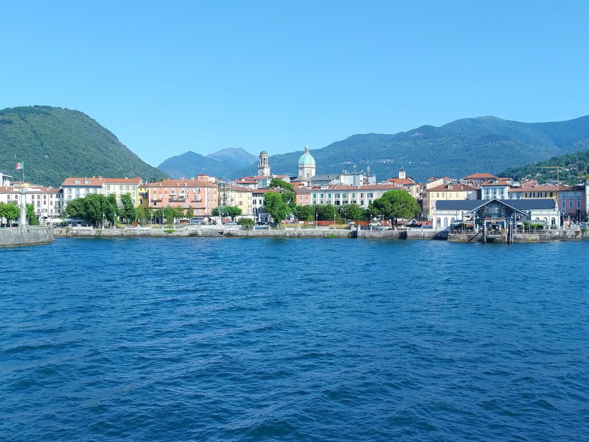 Une ville située au bord de l’eau, avec des bâtiments qui bordent la rivière, une imposante structure en forme de dôme et des montagnes en arrière-plan.