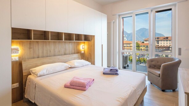 Un dormitorio moderno con una cama grande, cabecera de madera y vistas a un paisaje urbano a través de amplias ventanas.