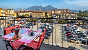 Un balcón con una mesa dispuesta para una comida, con vista a un estacionamiento y un paisaje urbano con montañas al fondo.