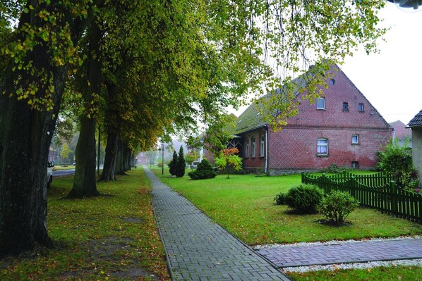 A brick building with a sloped roof, surrounded by a green fence and trees.