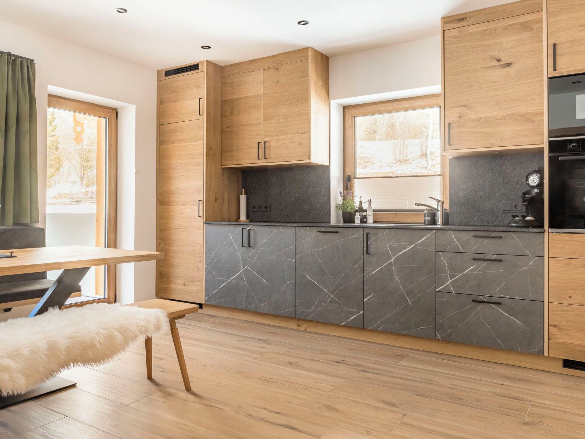Een moderne keuken met houten kastjes, een marmeren aanrecht en een eethoek met een zachte, witte bank.
