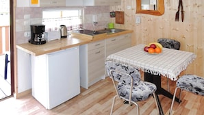 Una cocina compacta con un refrigerador pequeño, una cafetera y un lavamanos. Hay una mesa con mantel a cuadros y dos sillas con tapicería floral.
