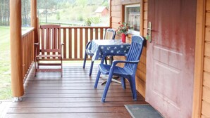 Una terraza de madera con una mesa y sillas, una puerta de madera, y vistas del entorno.
