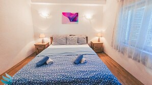 A bedroom with a bed, two bedside tables, a wall-mounted light, a window with blinds, and a colorful abstract painting above the bed. - Hvar spa & apartment-2 Bedroom-Terrace/Sea View 4 (Vrboska)
