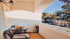 Un balcon avec une table et des chaises, un pot de fleurs et une vue sur un parc avec des arbres et des bâtiments.