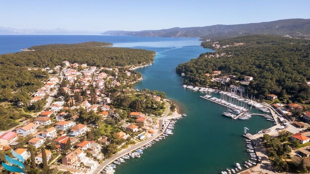 Vue aérienne d’une ville côtière avec des immeubles résidentiels, une marina et une mer d’un bleu limpide.