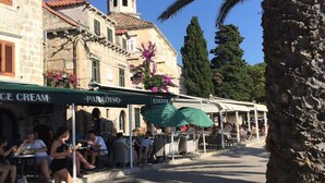 A street with outdoor seating at cafes, stone buildings, and a church tower.