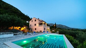 A swimming pool with lounge chairs, a building with a balcony, and a mountainous backdrop.
