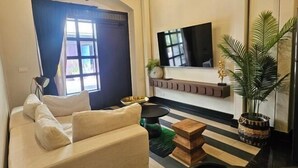 Un salon avec un canapé, un téléviseur fixé au mur, une plante en pot et un tapis à rayures.