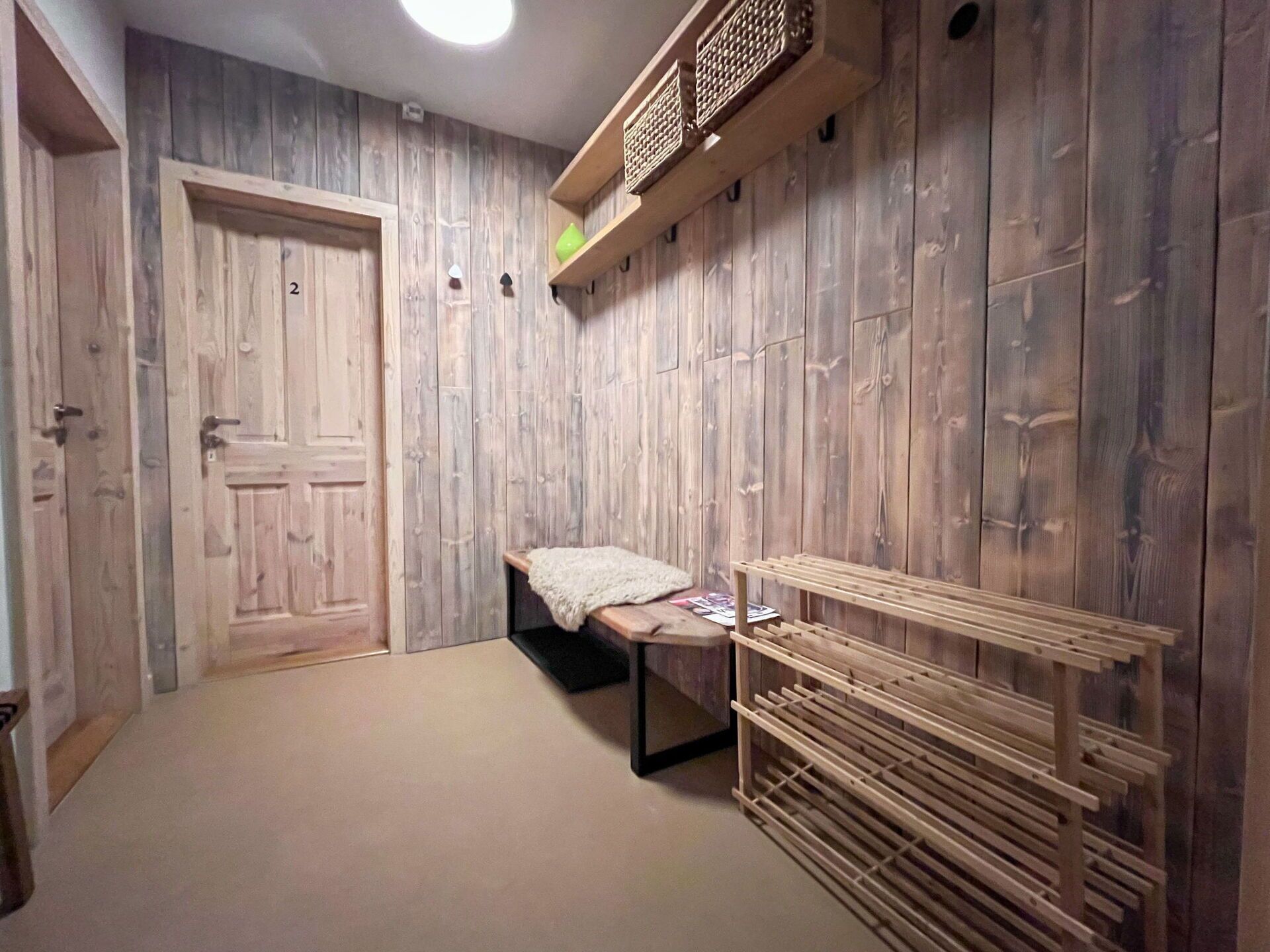 Ein Zimmer mit Holzwänden, einem Bett mit weißer Decke, einer hölzernen Bank und einem hängenden Holzregal.