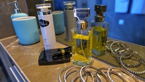Un tocador de baño con espejo, una botella de jabón de manos, una botella de crema hidratante y un juego de pulseras plateadas.