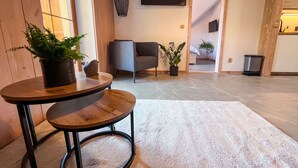 Ein modernes Wohnzimmer mit einem runden Holztisch, zwei Stühlen, einem grauen Sofa und Zimmerpflanzen.