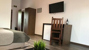 Una habitación de hotel moderna con cama, escritorio, silla, televisor y un refrigerador pequeño.