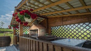An outdoor barbecue area with a brick oven, wooden deck, hanging flower baskets, and a view of the surrounding landscape. - Villa Rubčić - Double room with Terrace and Poold View - (8) (Rakovica)