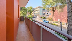 Un balcón con vista a una calle residencial, un coche estacionado y un árbol.