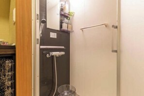 Un baño con ducha, un perchero y un recipiente de vidrio en el suelo.