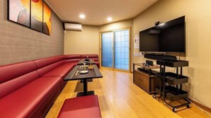 A room with a red sofa, a table with a remote control, a TV on a stand, and a sliding door.