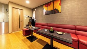 A modern dining area with a red leather booth, two tables with black bases, and a wall-mounted abstract painting.