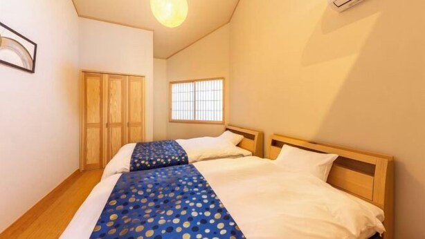 A bedroom with two beds, wooden headboards, a window with bars, and a hanging light fixture.