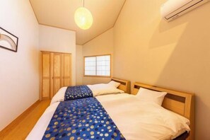 Een slaapkamer met twee bedden, houten hoofdeinden, een raam met tralies en een hanglamp.