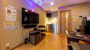 A modern living room with a flat-screen TV, wooden flooring, and a kitchen area with a microwave.