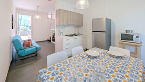 A compact kitchen with a gas stove, a refrigerator, and a microwave. There is a dining table with chairs and a patterned tablecloth.