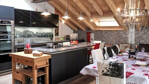 Une cuisine moderne dotée d’un îlot central, de poutres apparentes en bois au plafond et d’un lustre.