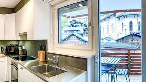 A modern kitchen with a stainless steel sink, a built-in oven, and a window overlooking a balcony with a table and chairs. - Lovely apartment for 6 people with WIFI, TV and balcony (Leukerbad)