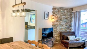 A cozy living room with a stone wall, a wooden dining table, a brown leather sofa, and a television. - Lovely apartment for 6 people with WIFI, TV and balcony (Leukerbad)