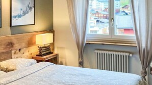 A bedroom with a large bed, a bedside table with a lamp, a framed picture on the wall, and a window with curtains. - Lovely apartment for 6 people with WIFI, TV and balcony (Leukerbad)