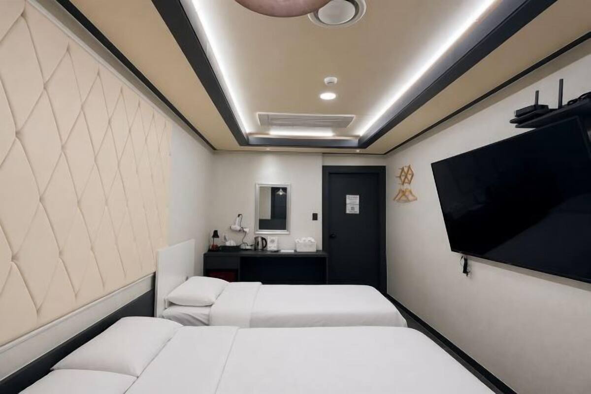 Quarto de hotel com duas camas, uma escrivaninha, televisão de tela plana e televisão montada na parede.