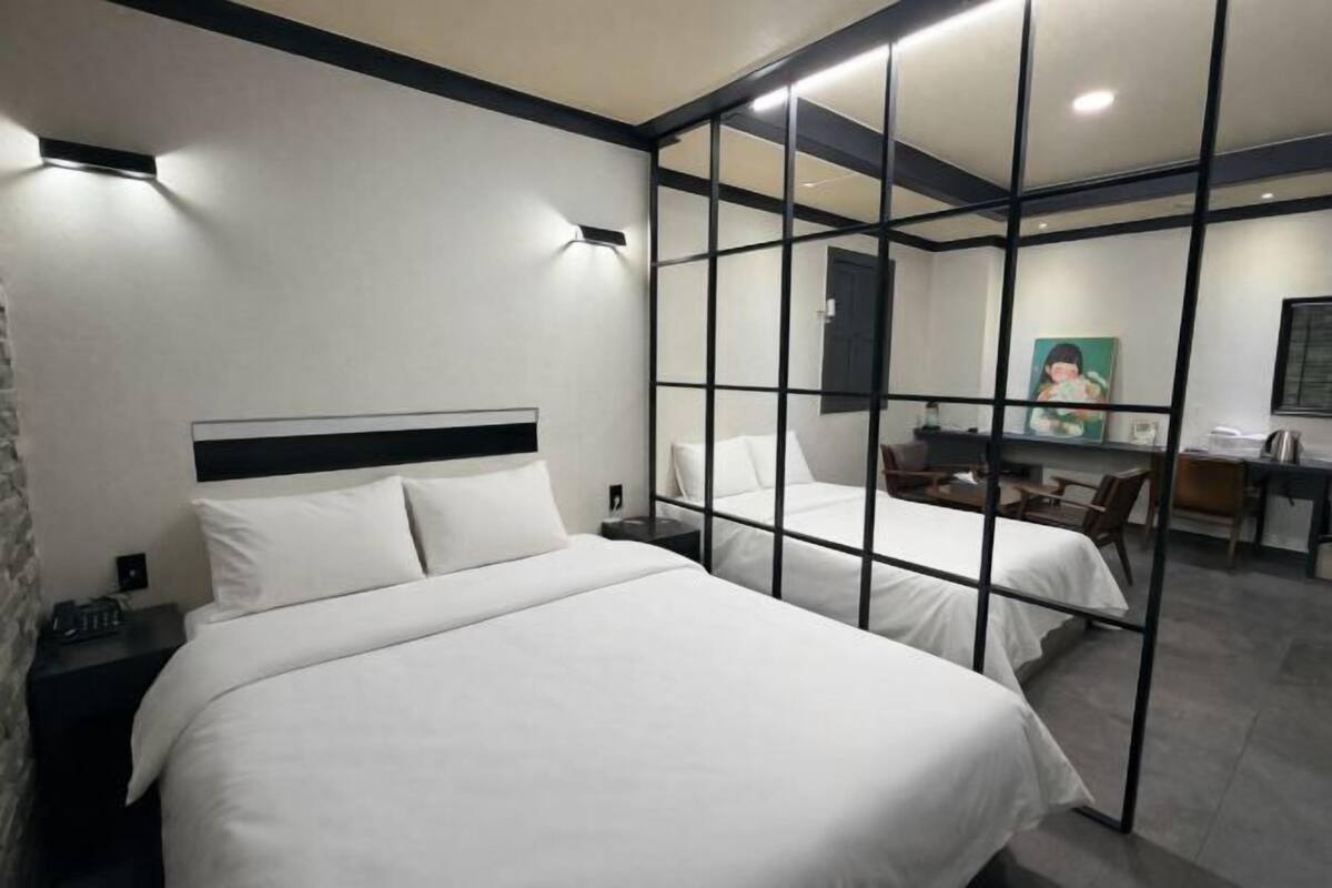 Quarto de hotel com duas camas, uma escrivaninha, uma cadeira e um espelho.
