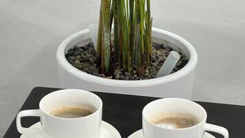 Two white cups on a tray, a potted plant with green leaves and a white pot, and a white wall in the background.