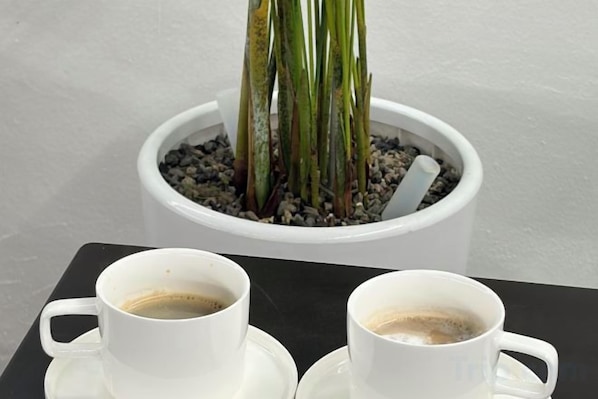 Two white cups on a tray, a potted plant with green leaves and a white pot, and a white wall in the background. - Carlton Hotel (Incheon)